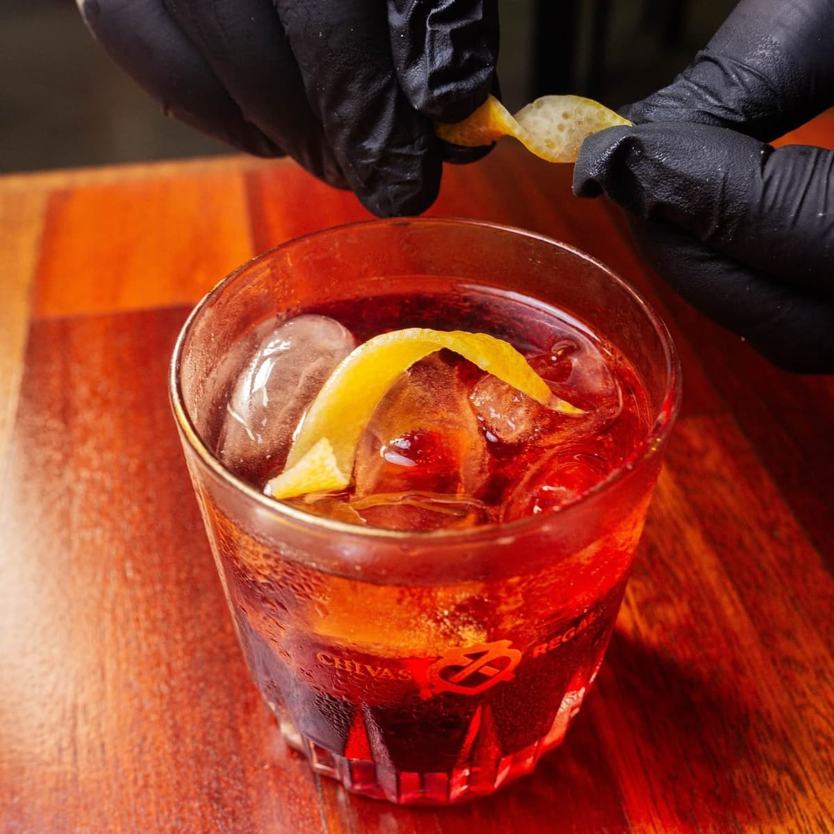 Bartender finalizando um drink com casca de laranja atrás do balcão