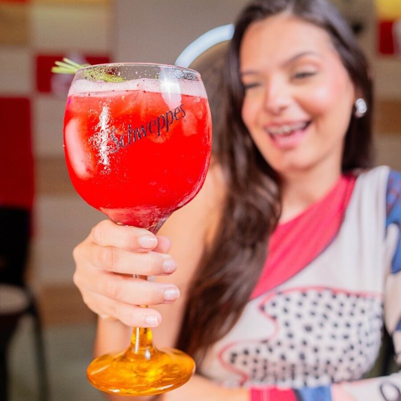Cliente erguendo um drink vermelho bem gelado na mesa do bar