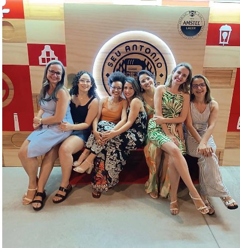 Grupo de amigas reunidas no banco em frente ao letreiro iluminado do Seu Antônio